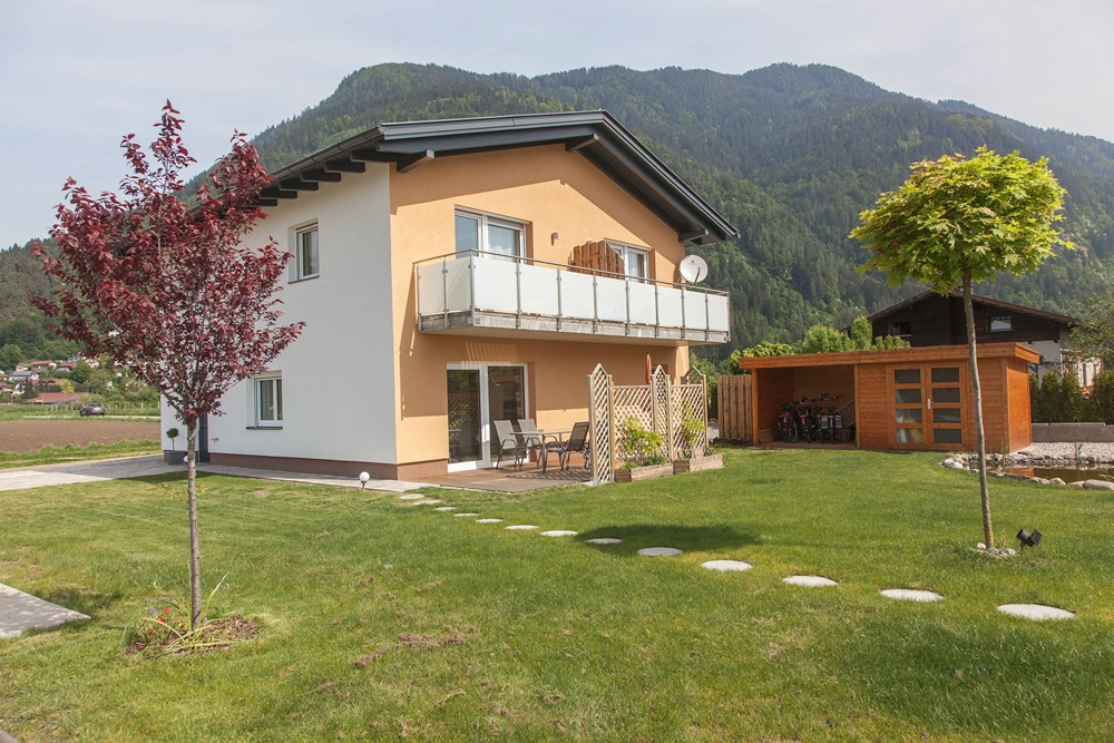 „Hahns Herberge“ – Außenansicht; stilvoll, gepflegter Garten mit Terasse und roten und grünen Baum.
